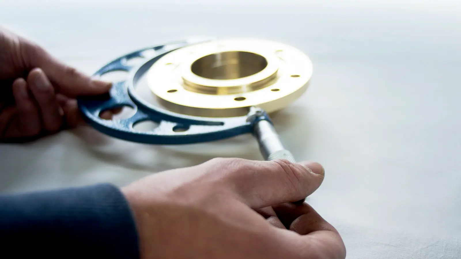 Hands measuring a brass flange with a micrometer during a teardown.