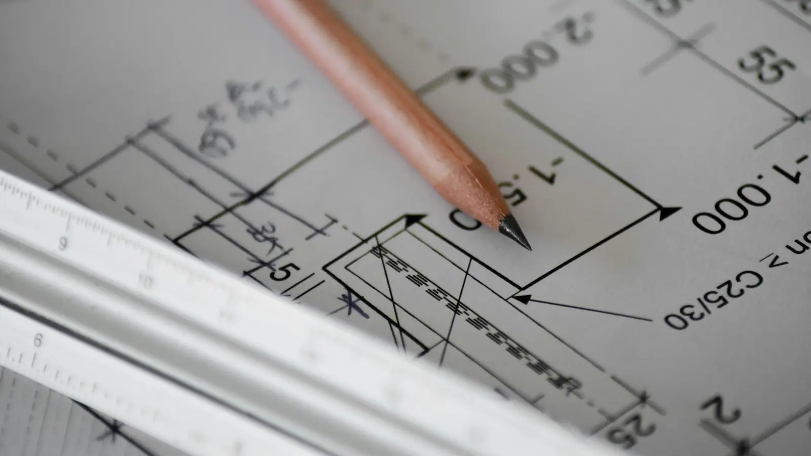 A pencil pointing at tolerance callouts on a technical drawing, next to a scale ruler.