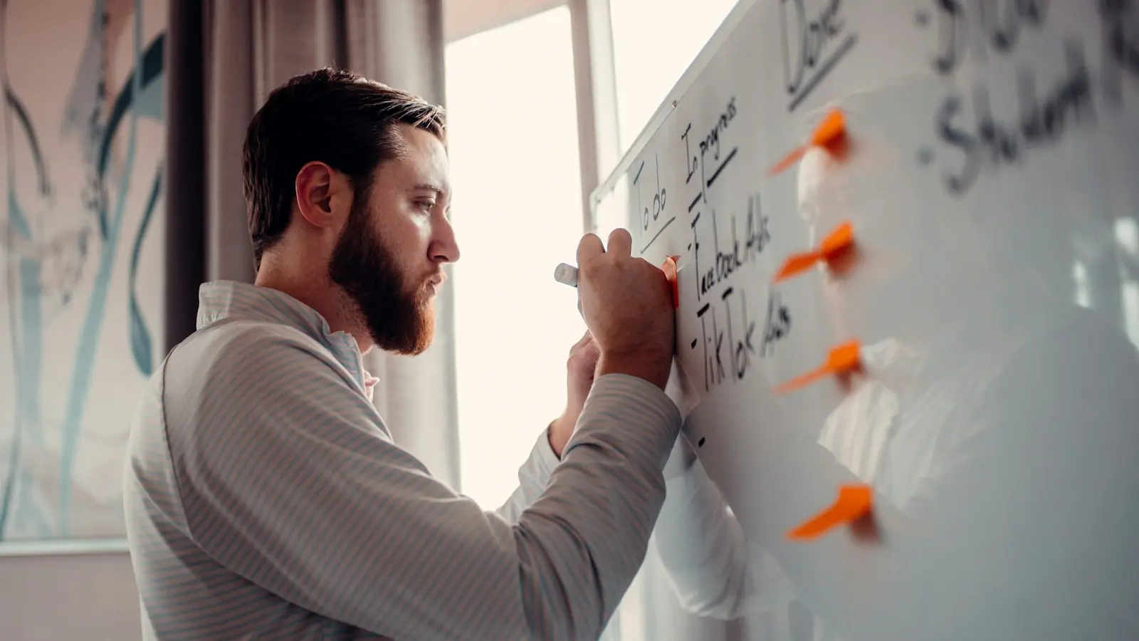 A procurement manager writing negotiation levers on a whiteboard, each marked with an orange magnet.