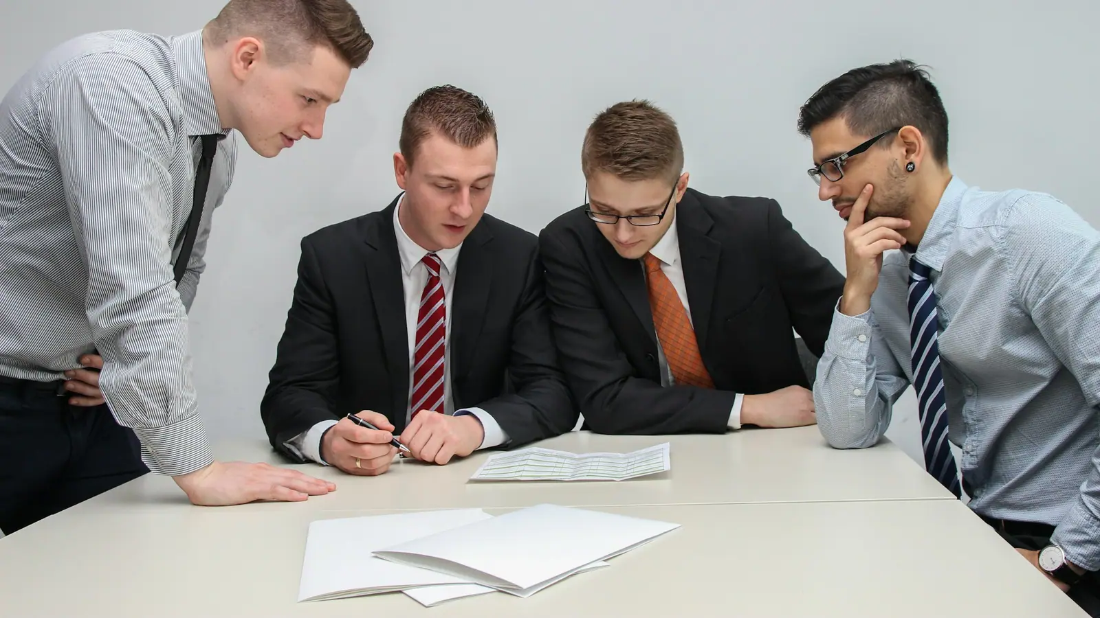 Four colleagues in a meeting room leaning over printed documents on a table.
