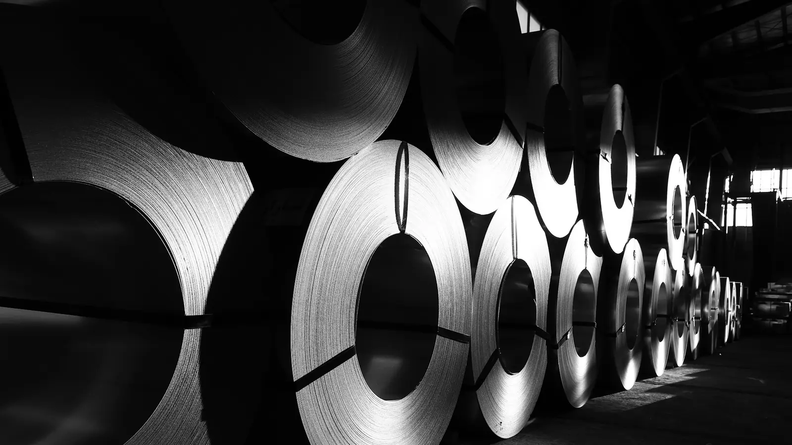 Rows of cold-rolled steel coils stored in a dimly lit warehouse.