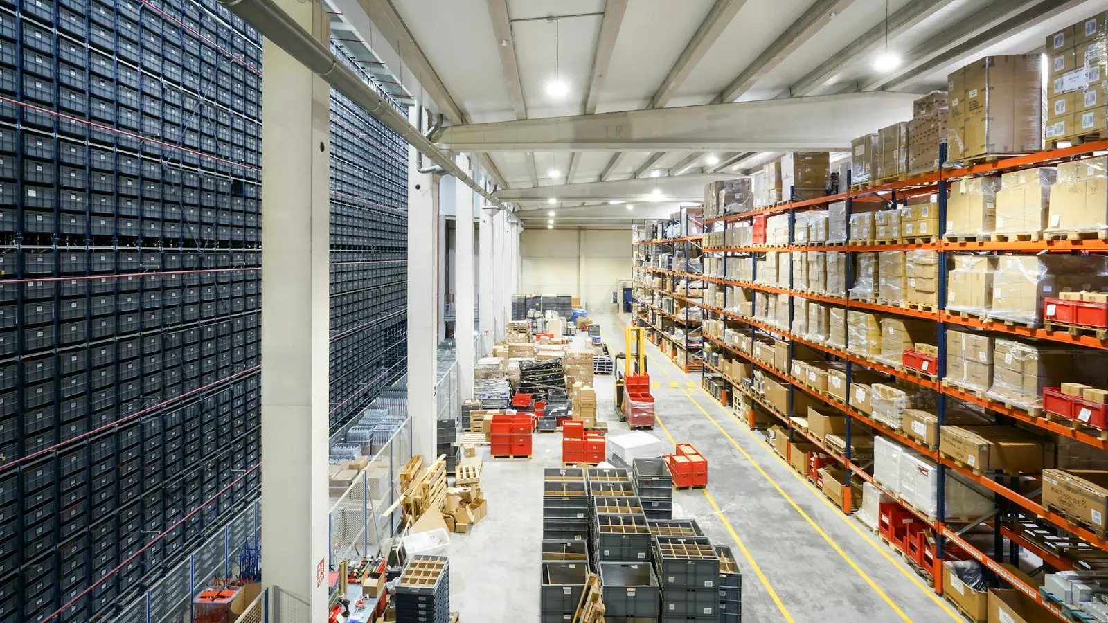A parts warehouse with a wall of small-part bins on one side and pallet racking on the other.