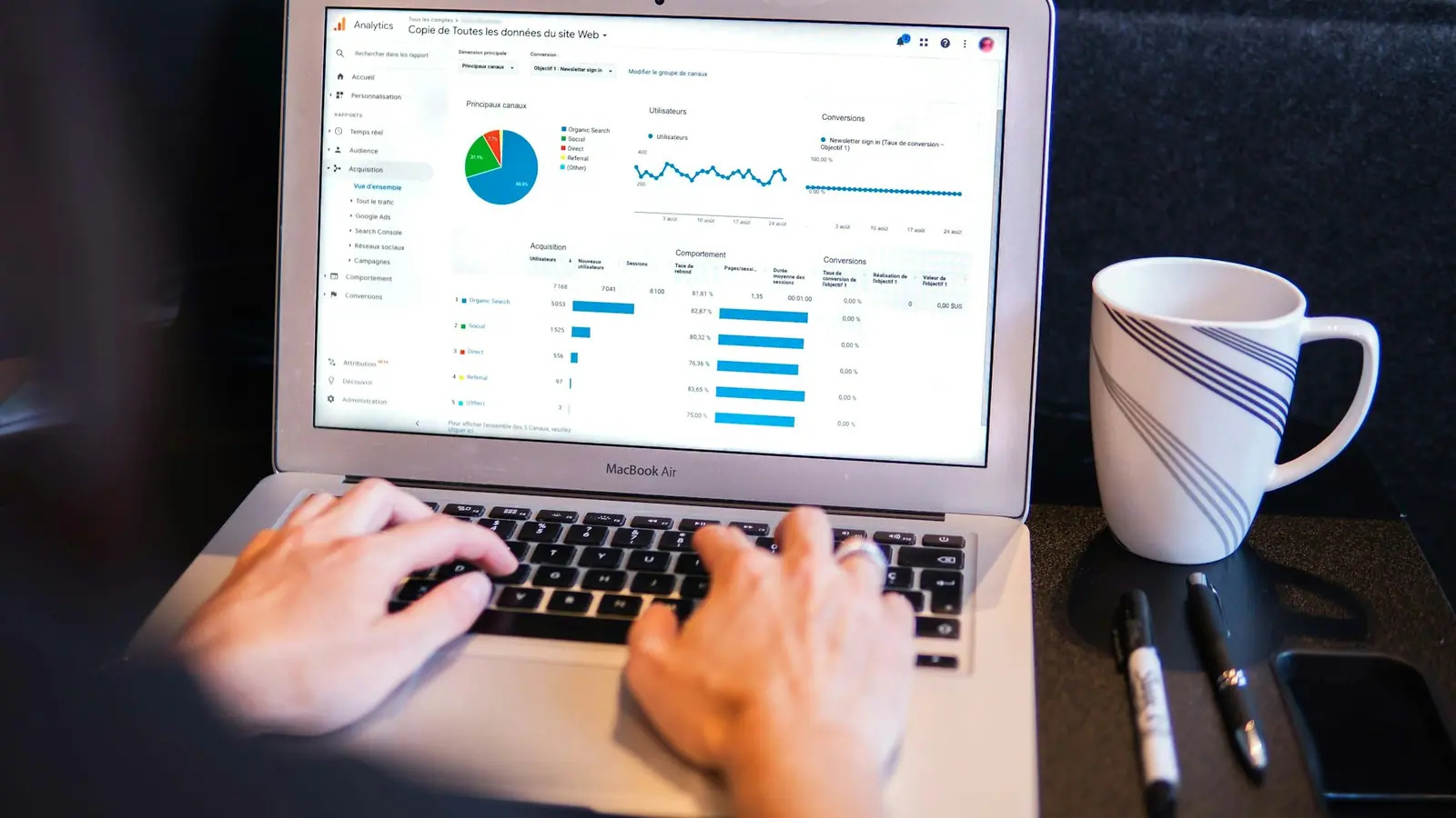 Hands typing on a laptop showing a spend dashboard with pie and bar charts.