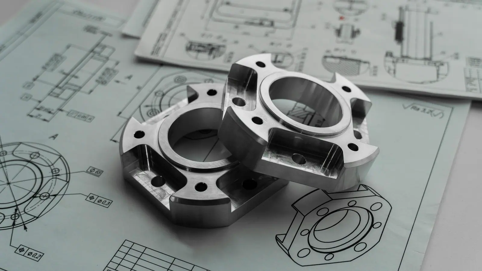 Two CNC-machined aluminium flanges resting on the engineering drawing they were made from.