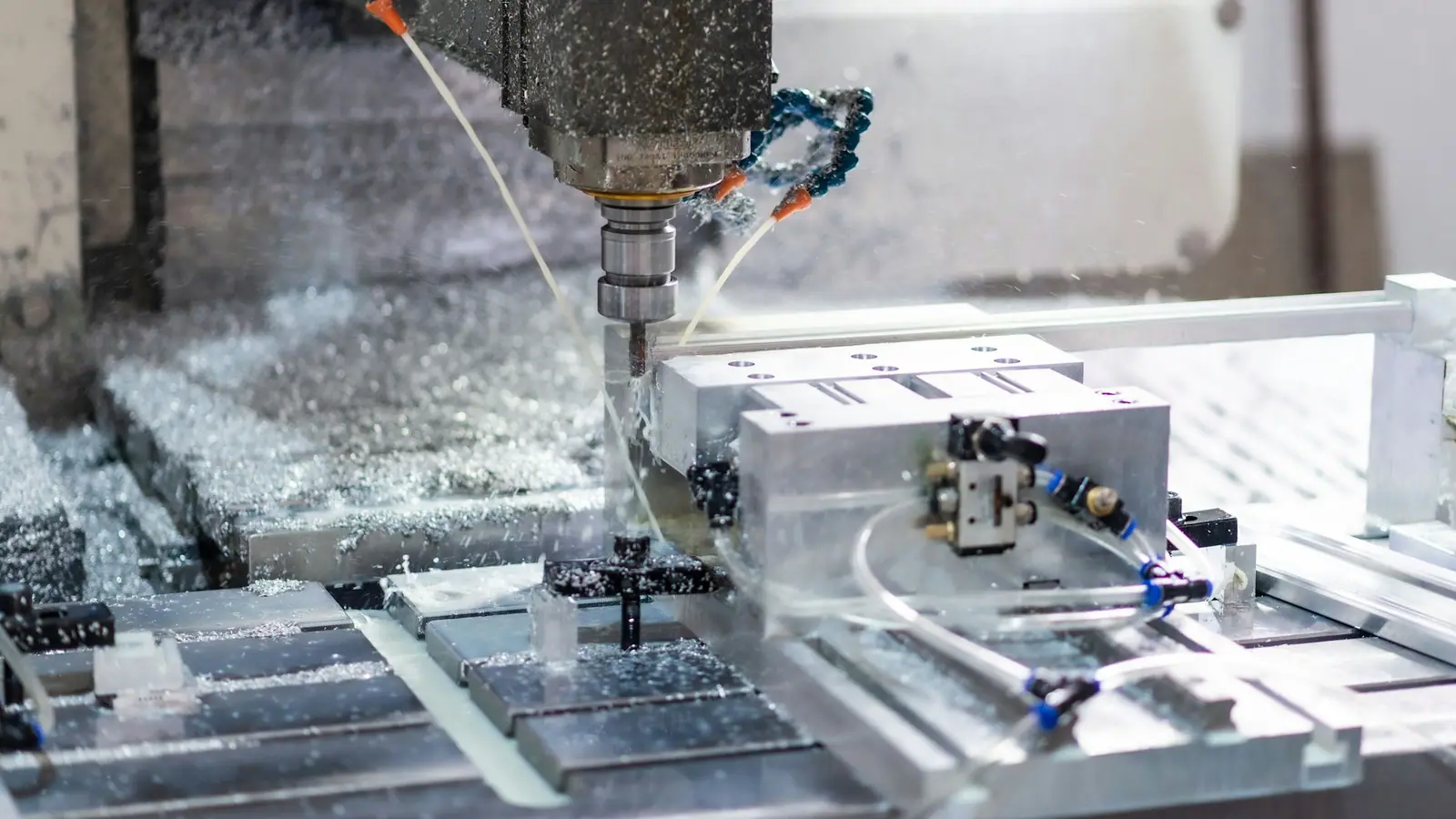 A CNC milling cutter machining an aluminium block, with coolant spraying over the chips.