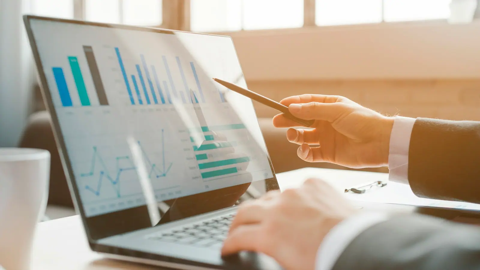 A buyer pointing a pen at cost charts on a laptop screen.